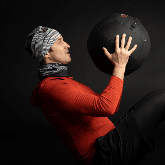 A man in athletic wear wearing a Dark Steel beanie and neck gaiter while lifting a medicine ball.