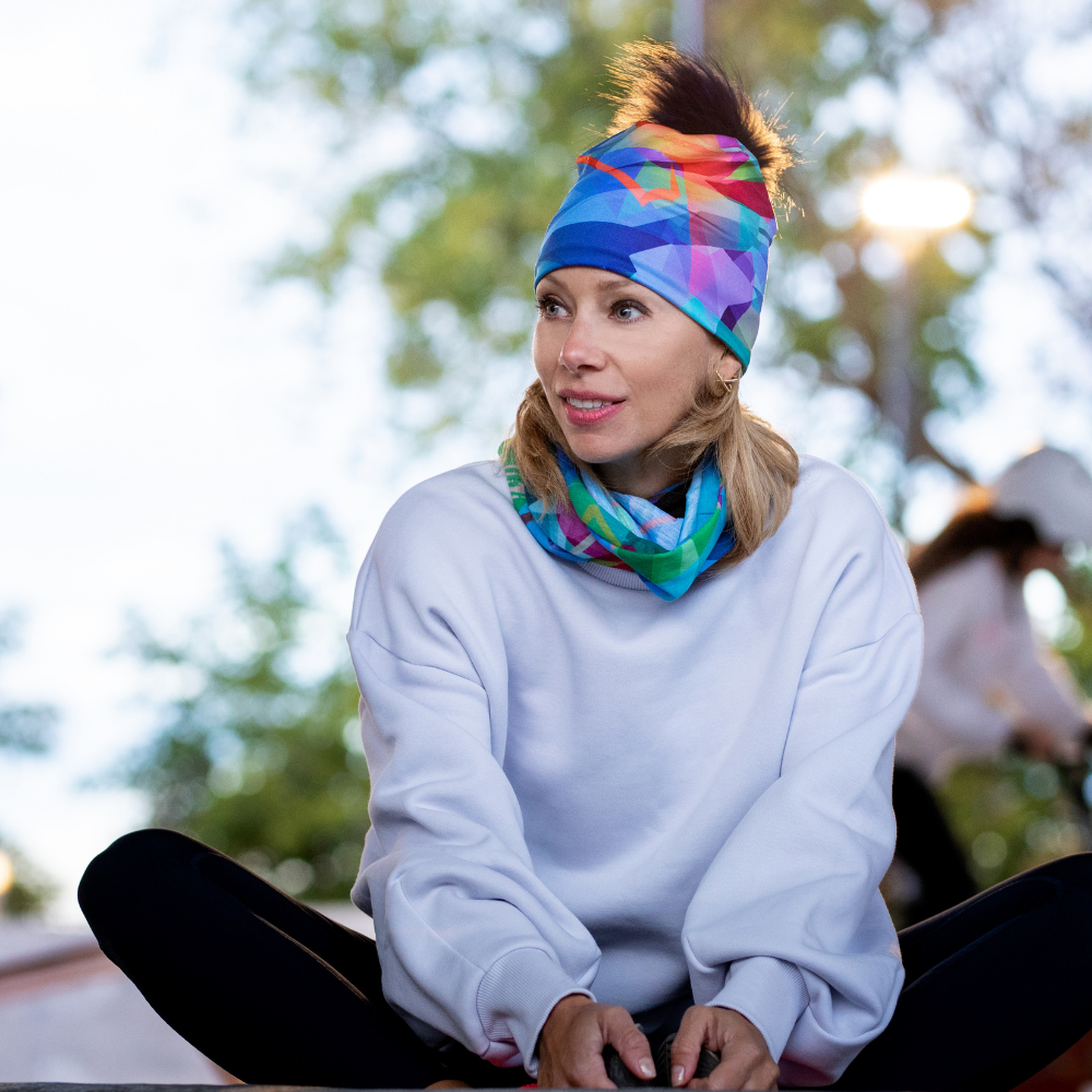 Femme portant un sweat à capuche blanc et le tube de cou au motif abstrait comme bandeau et autour de son cou.