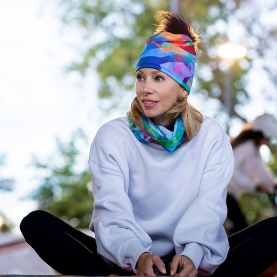 Femme portant un sweat à capuche blanc et le tube de cou au motif abstrait comme bandeau et autour de son cou.