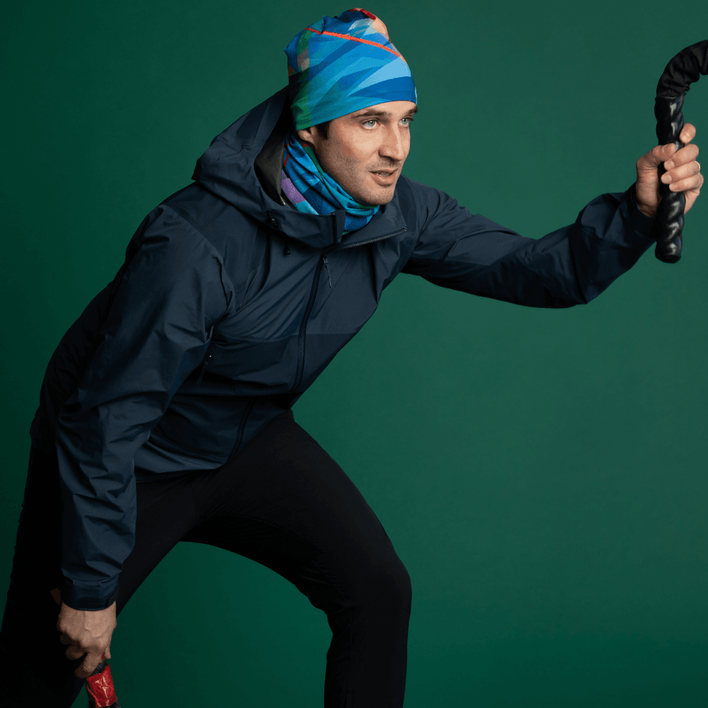 Man wearing a blue jacket and a matching 'Fast Triangles' neck tube and beanie, holding a fitness rope.