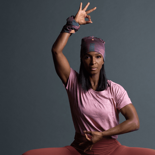 Une femme en t-shirt rose et legging corail démontre le port du bandana à motif géométrique violet comme bandeau et poignet éponge.