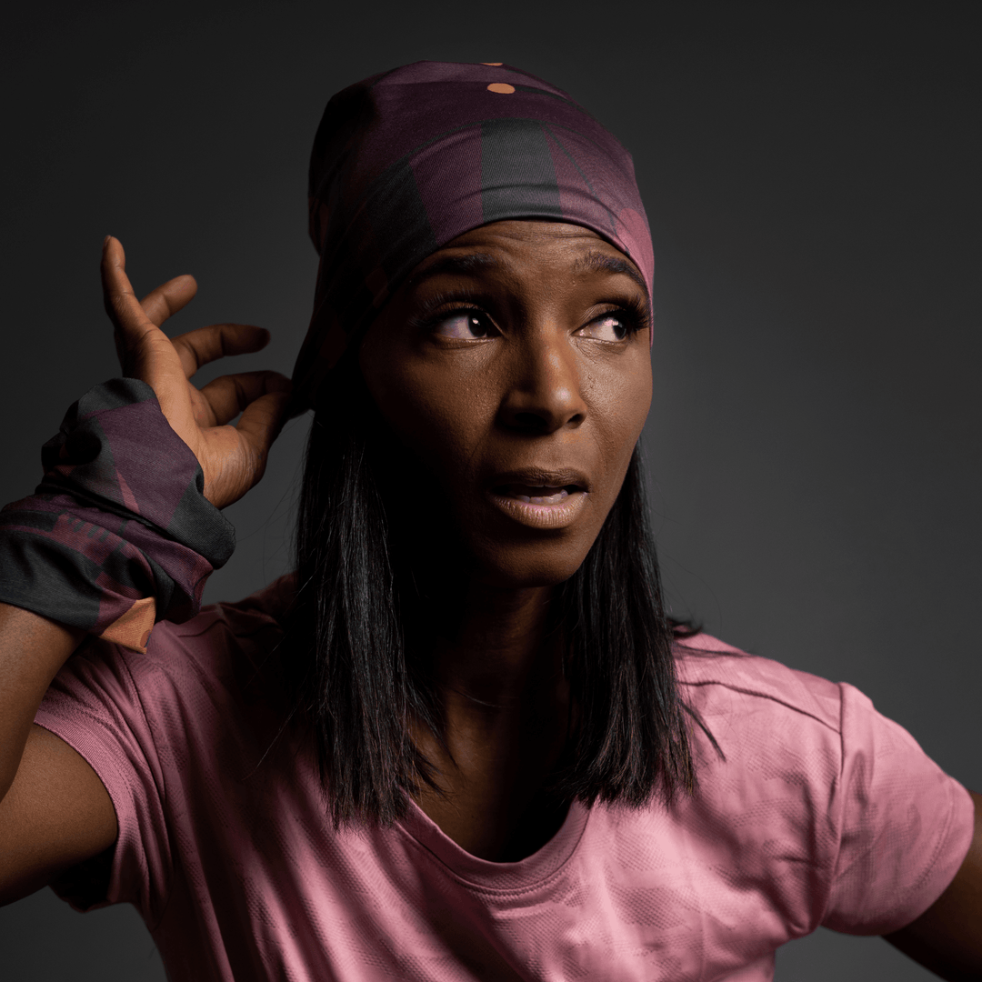 Une femme en t-shirt rose ajuste le bandana à motif géométrique violet sur sa tête, regardant sur le côté.