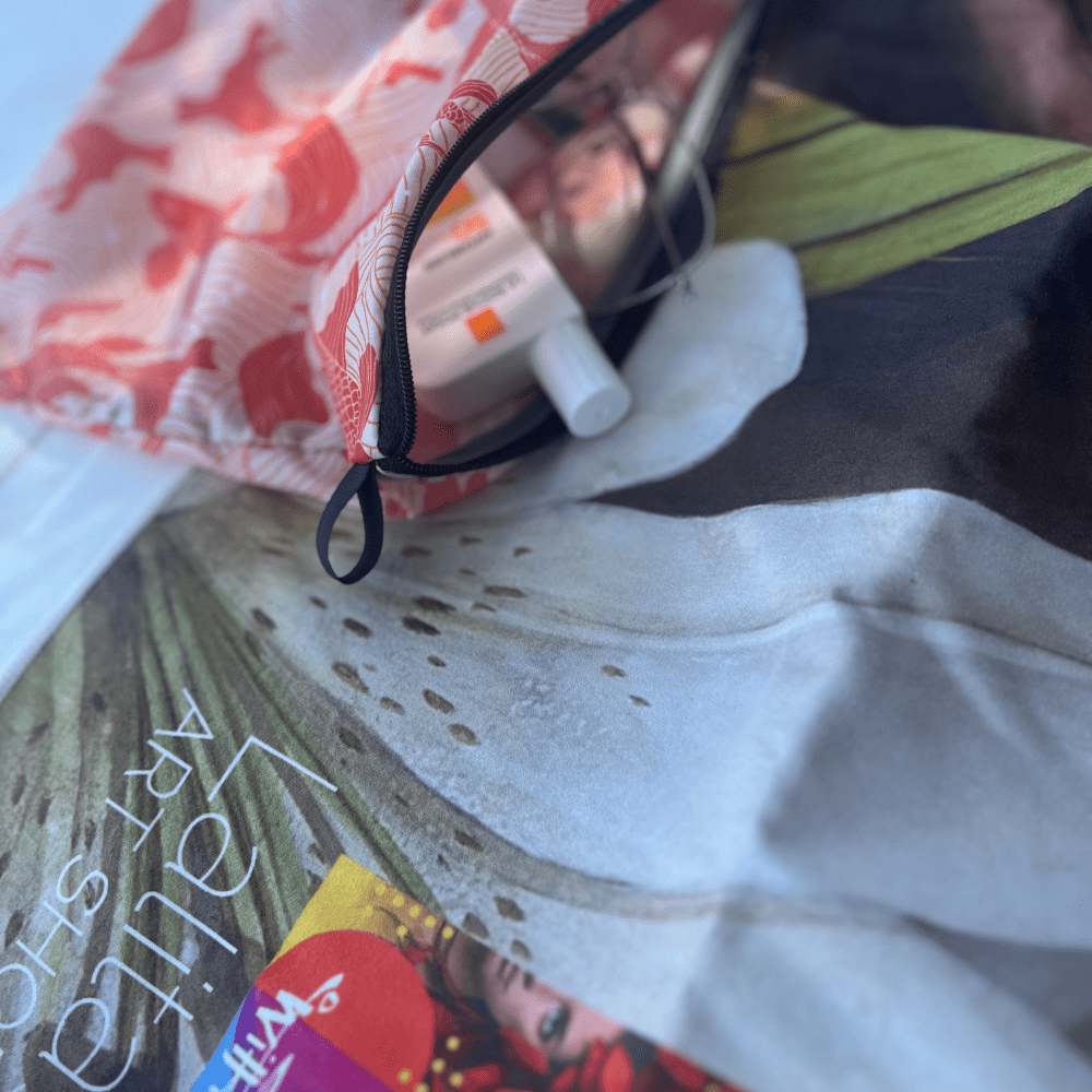 Gros plan de la serviette Guerrière Pacifique et de sa pochette incluse, montrant de la crème solaire et des articles de toilette.