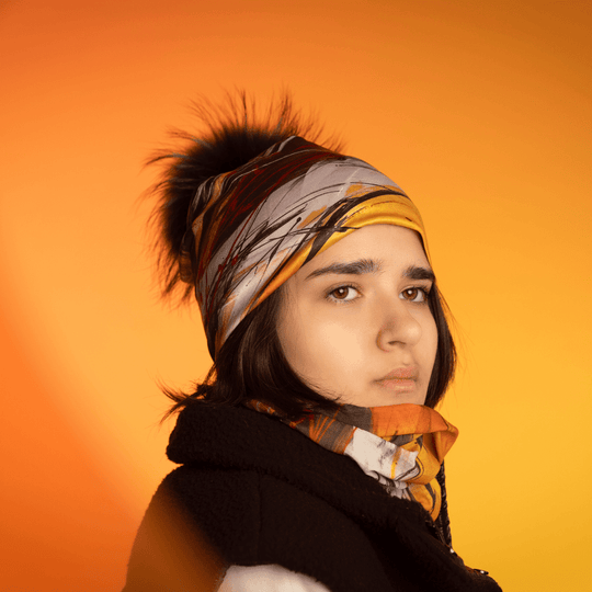 Une jeune femme porte la tuque Le Coeur avec son cache-cou assorti, sur un fond orange chaud.