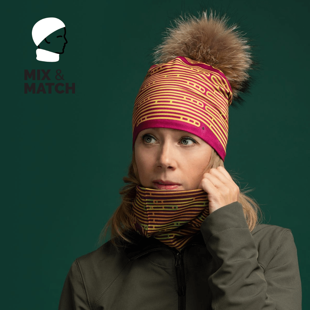 Femme portant une tuque et un cache-cou assortis magenta et jaune rayés, avec une veste verte sur fond vert foncé.