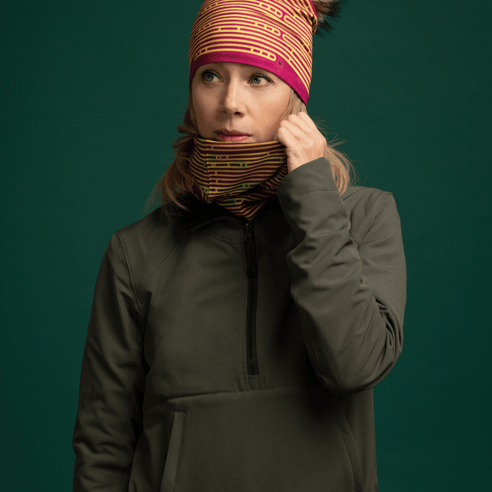 Femme portant une veste vert foncé, ajustant un Tube multifonctionnel Magenta autour de son cou, lequel présente un motif abstrait coloré.