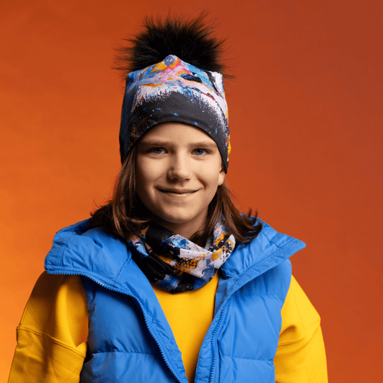 Une jeune personne souriante portant la tuque MatriX et le cache-cou assorti, sous un veston bleu et une chemise jaune.