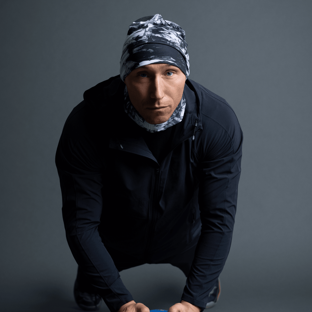 Homme en veste noire, portant une tuque et un cache-cou au motif abstrait noir et blanc, en pose pompe.