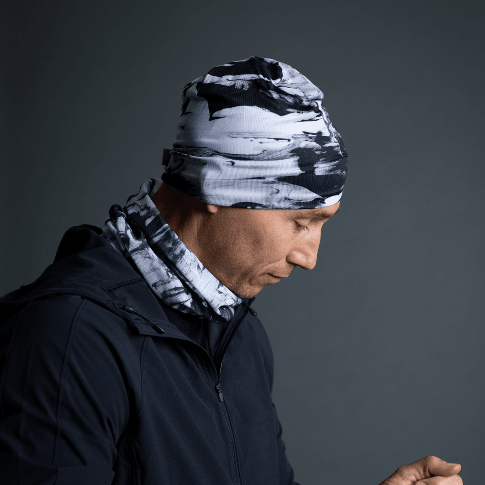 Homme portant une tuque et un cache-cou assorti au motif abstrait noir et blanc, avec une veste noire.