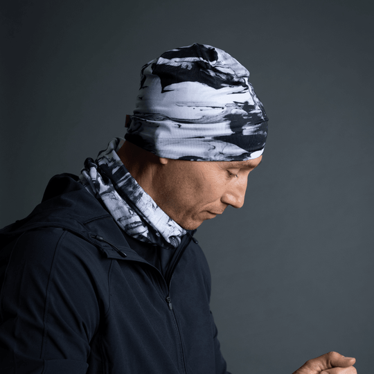Homme portant une tuque et un cache-cou assorti au motif abstrait noir et blanc, avec une veste noire.