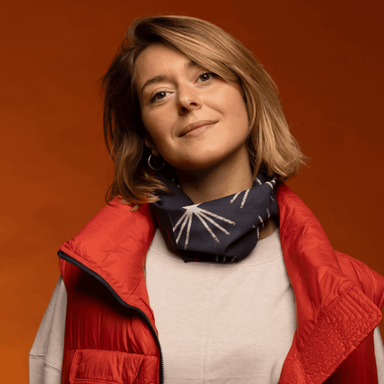 Une femme portant un gilet rouge et un tube à motif étoile négligemment autour du cou.