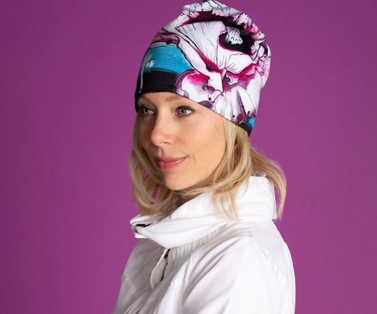 Woman wearing the New Poppy Beanie, which features a colourful floral design and a black pom pom.