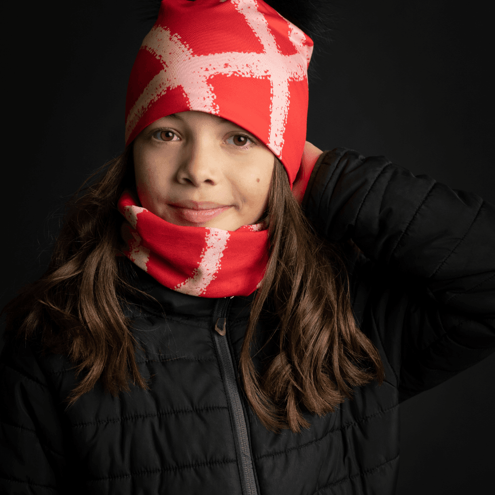 Young girl wearing a red beanie with abstract peach pattern and matching neck warmer, dressed in a black puffer jacket.