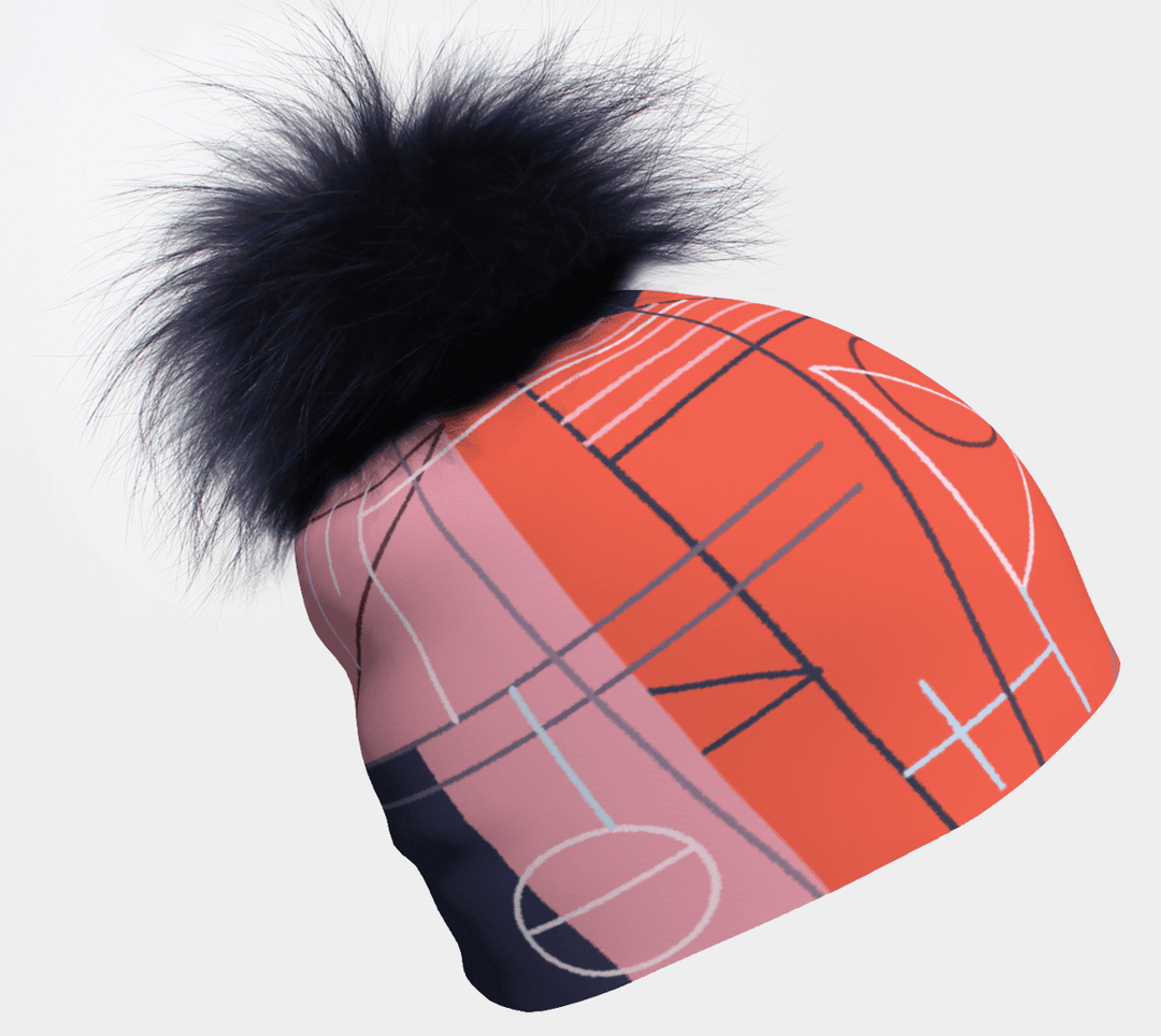 Gros plan d'une tuque avec un imprimé graphique abstrait rose, bleu et orange, avec un grand pompon bleu marine détachable.
