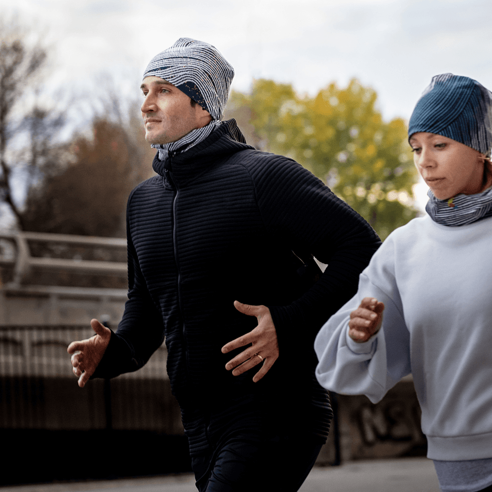 Homme et femme portant des tubes multifonctionnels POLAR Dark Steel assortis en tuques et cache-cous tout en courant à l'extérieur.