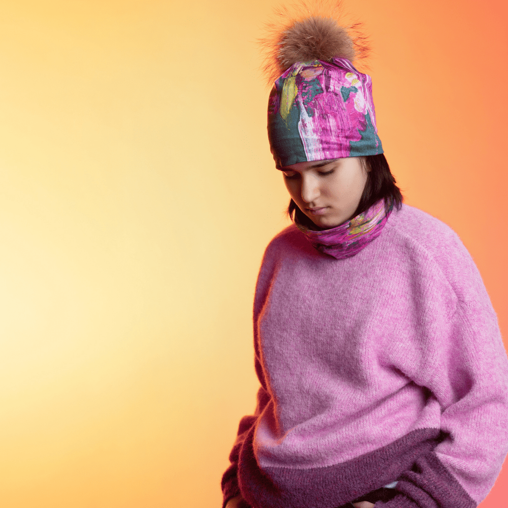 A young person wearing a pink sweater and a beanie and neck warmer with abstract floral art.