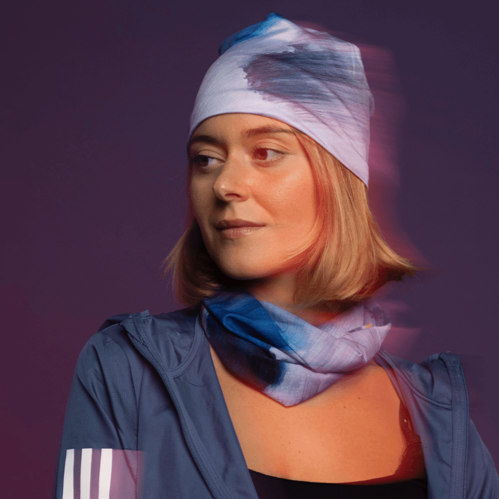 Une femme portant une veste bleue et un bandana "Mer Dorée" assorti comme bandeau et tour de cou, avec un effet de flou.