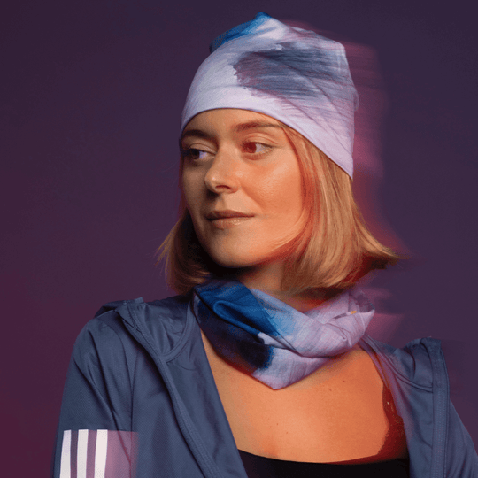 Une femme portant une veste bleue et un bandana "Mer Dorée" assorti comme bandeau et tour de cou, avec un effet de flou.