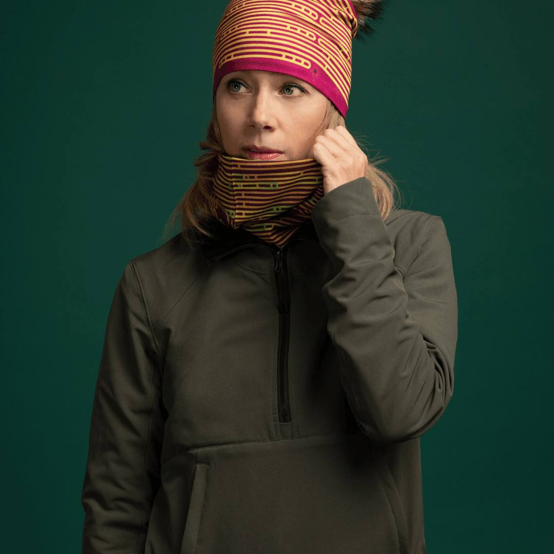 Femme portant une veste verte et un tube à motif, touchant le tissu près de son cou.