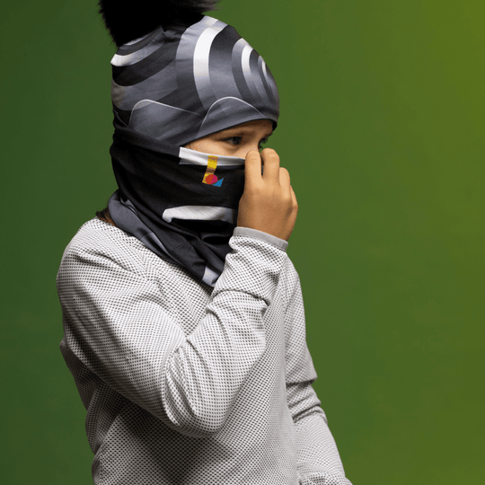 Child wearing a grey waffle-knit shirt and a black and grey abstract print neck tube pulled up as a face covering.