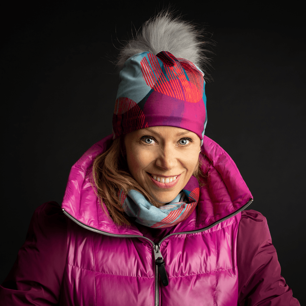 Une femme souriante portant une veste rose épaisse et un ensemble assorti de tuque et foulard avec le motif Pois turquoise.