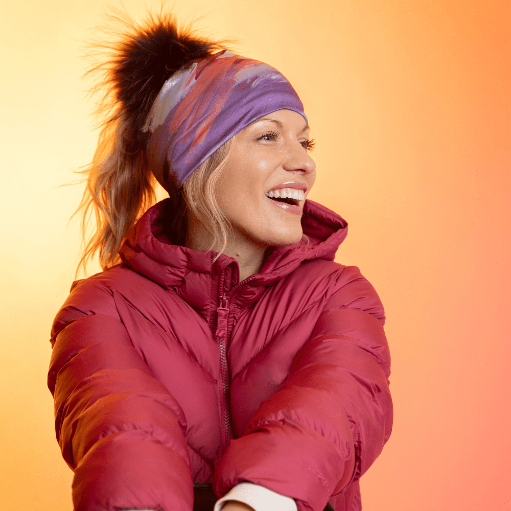 Woman wearing the Ponytail Tulips Beanie with a black pompom and a red puffer jacket, laughing.
