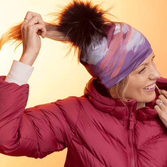 Woman wearing the Ponytail Tulips Beanie with a black pompom, a red puffer jacket, and a ponytail.