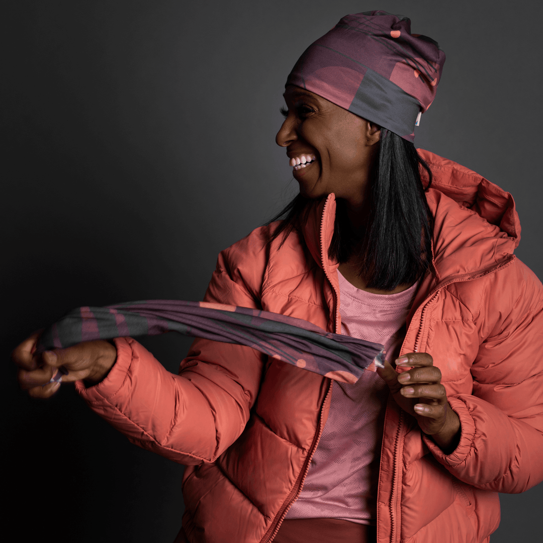 Femme en veste matelassée corail tenant un tube Motifs Géométriques Mauves, souriant.