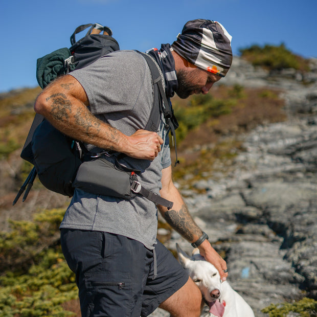 Man hiking with his dog, wearing Lalita's Art Shop Samouraï Beanie and Tube for outdoor adventures.