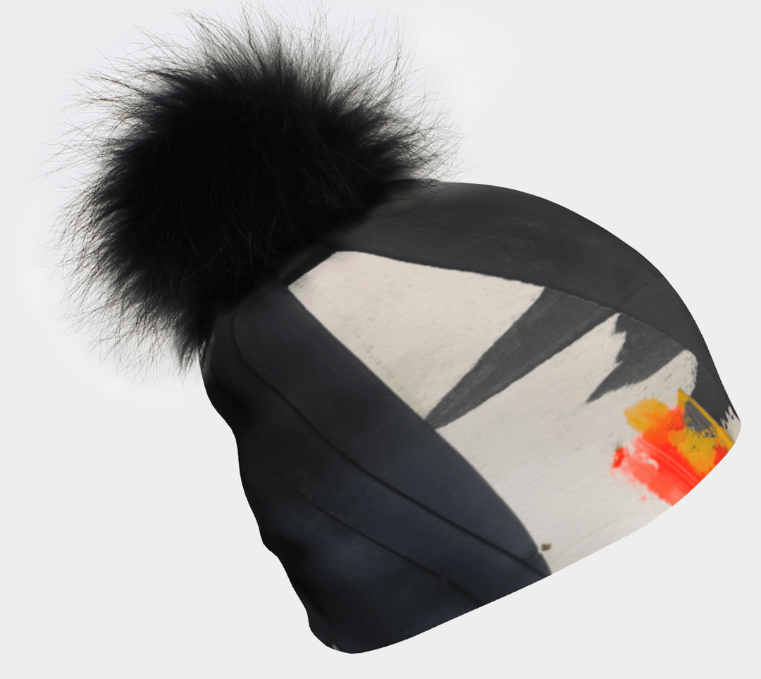Gros plan d'une tuque noire avec art abstrait monochrome et éclaboussures orange et jaune, surmontée d'un gros pompon noir moelleux.