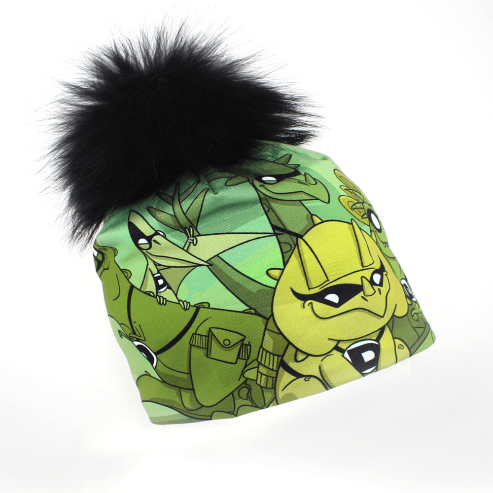 Tuque verte avec un pompon noir et moelleux, décorée d'illustrations de dinosaures de dessin animé.