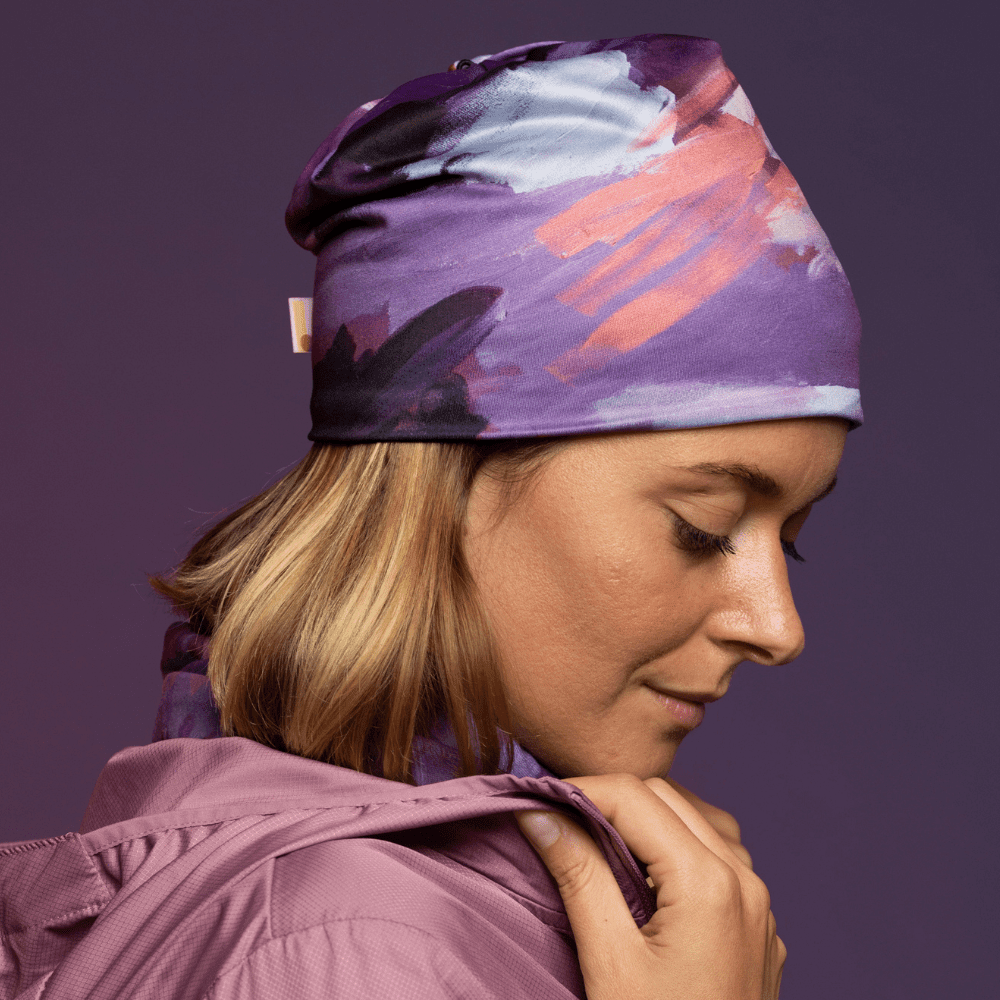 Femme portant une tuque à motif abstrait violet et un cache-cou assorti, avec une veste rose.