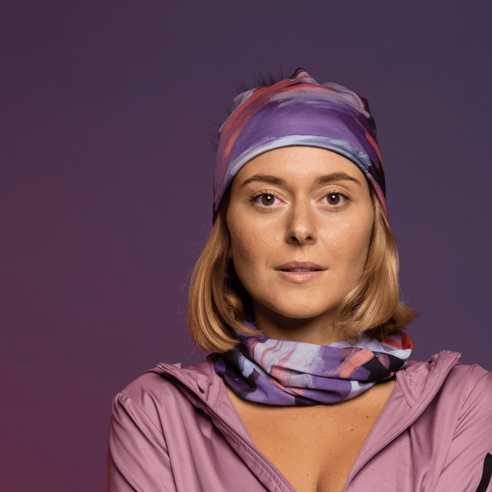 Une femme porte une tuque et un tube assortis avec un imprimé floral, posant sur fond violet.