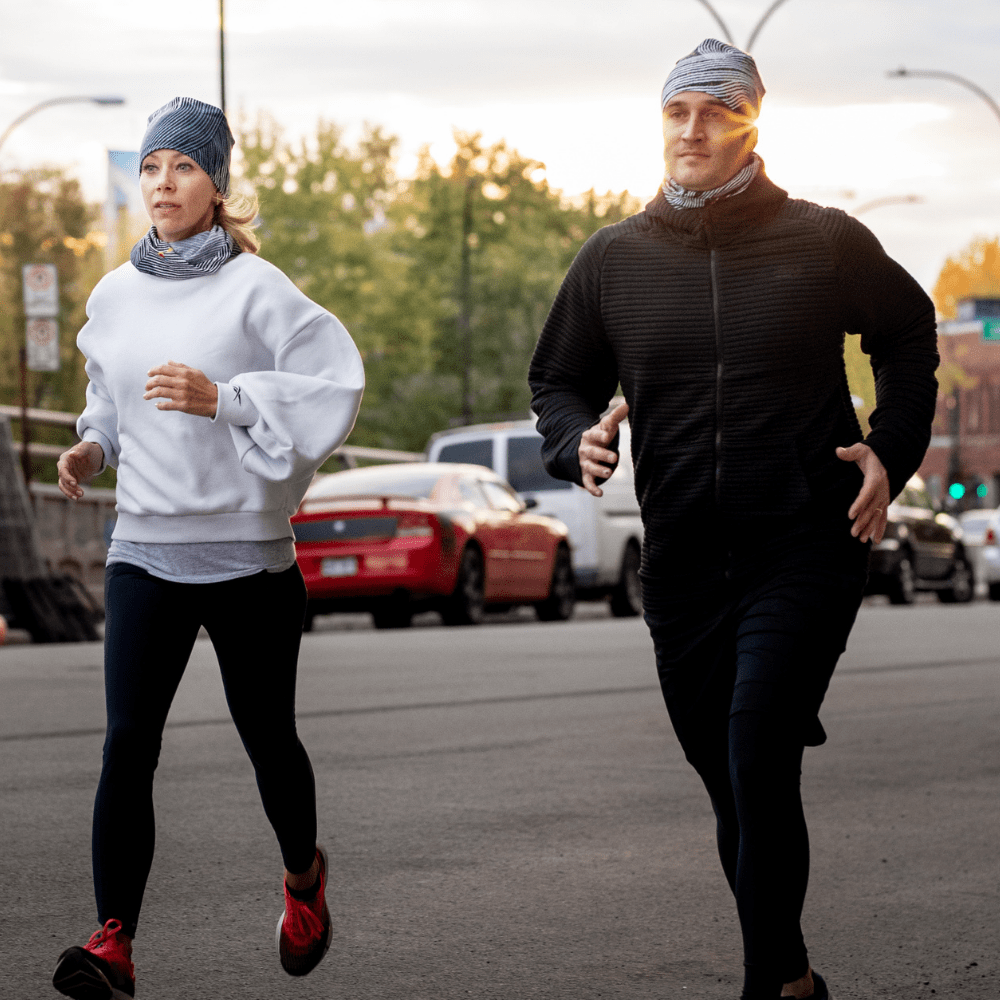 Un homme et une femme courant dehors au coucher du soleil, portant tous deux des tuques et cache-cous assortis à rayures abstraites.
