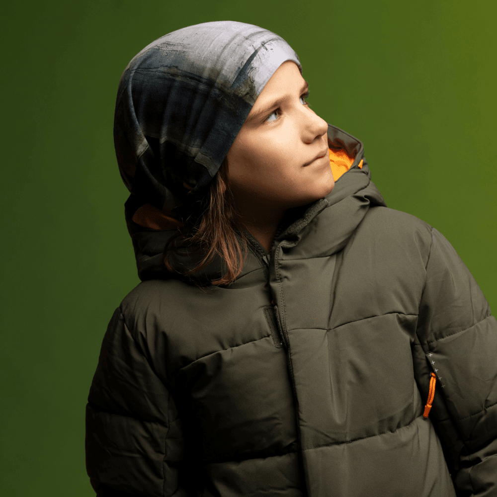Jeune garçon regardant sur le côté, portant le Tube Multifonction Murale en tuque avec une veste matelassée verte.
