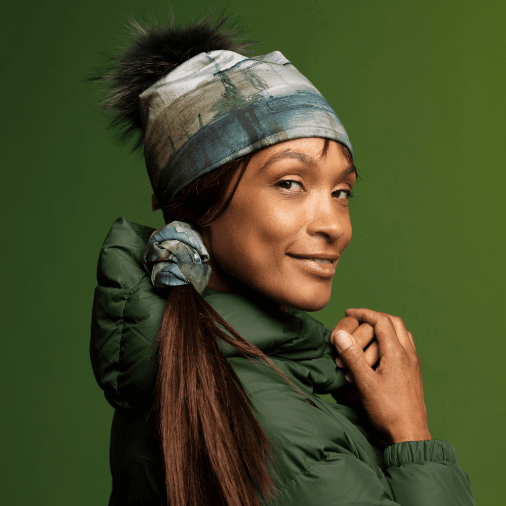 Une femme portant une tuque Murale et un cache-cou comme accessoire pour cheveux, avec une veste matelassée verte.