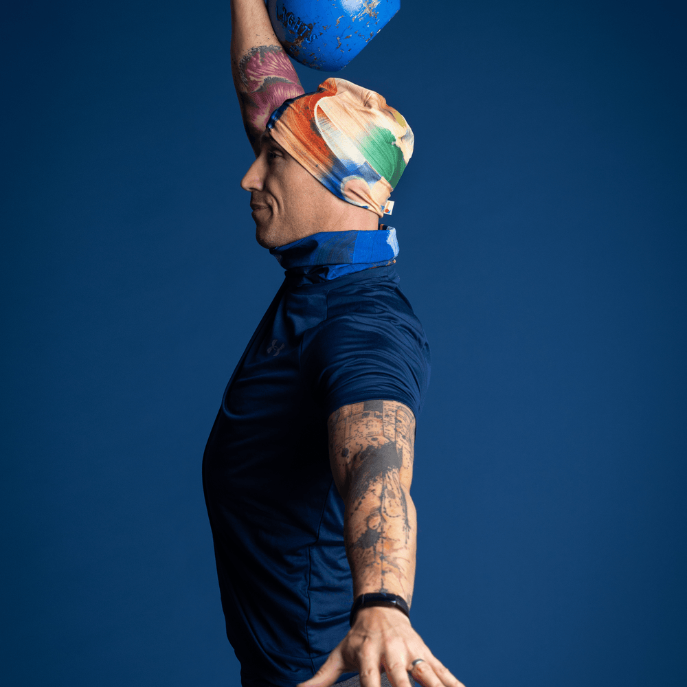 Homme portant la tuque à art abstrait jaune et bleu et le cache-cou assorti, effectuant un épaulé-jeté avec kettlebell.