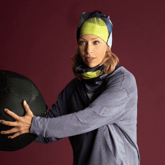 Une femme portant le tube multifonctionnel Pois Jaunes comme bandeau et cache-cou, tenant un gros ballon d&